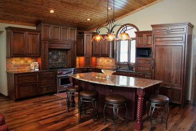 This is an example of a large country l-shaped eat-in kitchen in Minneapolis with a drop-in sink, recessed-panel cabinets, dark wood cabinets, granite benchtops, multi-coloured splashback, porcelain splashback, stainless steel appliances, dark hardwood floors and with island.