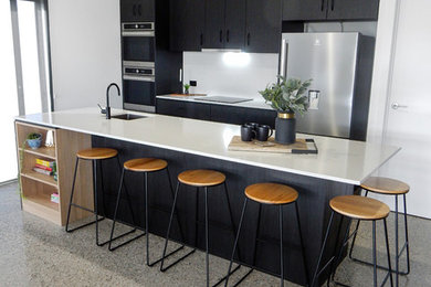 This is an example of a large transitional galley open plan kitchen in Other with an undermount sink, recessed-panel cabinets, black cabinets, quartz benchtops, white splashback, stone slab splashback, stainless steel appliances, concrete floors, with island, multi-coloured floor and white benchtop.