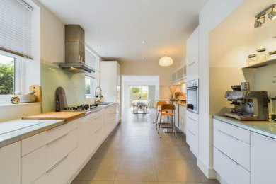 Photo of a large modern grey and white galley kitchen/diner in Other with a built-in sink, flat-panel cabinets, white cabinets, laminate countertops, green splashback, glass sheet splashback, stainless steel appliances, ceramic flooring, grey floors, green worktops, a drop ceiling and feature lighting.