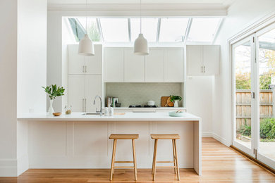 Photo of a mid-sized contemporary galley eat-in kitchen in Melbourne with a drop-in sink, shaker cabinets, white cabinets, quartzite benchtops, ceramic splashback, stainless steel appliances, light hardwood floors, with island and white benchtop.