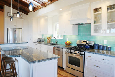 Design ideas for a mid-sized beach style l-shaped open plan kitchen in San Diego with an undermount sink, recessed-panel cabinets, white cabinets, granite benchtops, green splashback, ceramic splashback, stainless steel appliances, medium hardwood floors, with island and brown floor.