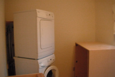 Ejemplo de lavadero multiusos actual grande con fregadero encastrado, armarios con paneles lisos, encimera de laminado, paredes grises, suelo de baldosas de porcelana y lavadora y secadora escondidas