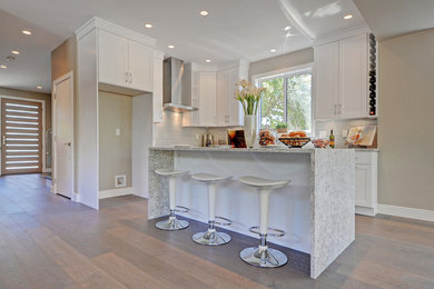 Inspiration for a mid-sized transitional l-shaped open plan kitchen in Vancouver with shaker cabinets, white cabinets, quartz benchtops, with island, white splashback, glass tile splashback, an undermount sink, light hardwood floors, stainless steel appliances and brown floor.