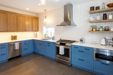 This is an example of a transitional kitchen with an undermount sink, shaker cabinets, blue cabinets, quartz benchtops, white splashback, porcelain splashback, stainless steel appliances, ceramic floors, brown floor and white benchtop.