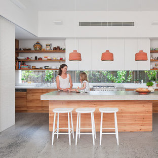 This is an example of a medium sized contemporary galley kitchen in Melbourne with a submerged sink, flat-panel cabinets, white cabinets, concrete worktops, glass sheet splashback, stainless steel appliances, concrete flooring and an island.