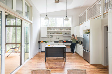 Inspiration for a small modern l-shaped medium tone wood floor and brown floor open concept kitchen remodel in Charlotte with a farmhouse sink, recessed-panel cabinets, white cabinets, wood countertops, white backsplash, stainless steel appliances and an island