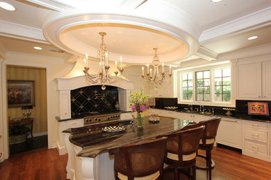 Eat-in kitchen - mid-sized traditional u-shaped medium tone wood floor and brown floor eat-in kitchen idea in Other with a double-bowl sink, raised-panel cabinets, white cabinets, granite countertops, black backsplash, stone slab backsplash, stainless steel appliances and an island