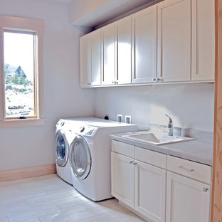 Large traditional single-wall utility room in Seattle with a built-in sink, shaker cabinets, white cabinets, tile countertops, grey walls, porcelain flooring, a side by side washer and dryer and grey worktops.