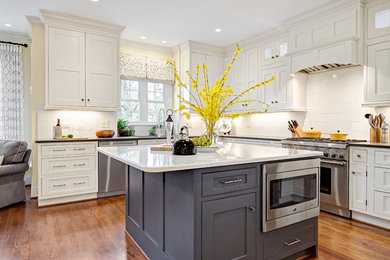 Example of a large transitional u-shaped medium tone wood floor and brown floor eat-in kitchen design in Other with an undermount sink, shaker cabinets, white cabinets, quartz countertops, white backsplash, porcelain backsplash, stainless steel appliances and an island