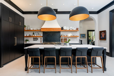 На фото: угловая кухня в стиле неоклассика (современная классика) с врезной мойкой, черными фасадами, черным фартуком, островом, серым полом и белой столешницей с