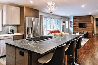 Inspiration for a large 1950s u-shaped medium tone wood floor open concept kitchen remodel in Other with an undermount sink, flat-panel cabinets, medium tone wood cabinets, soapstone countertops, green backsplash, ceramic backsplash, stainless steel appliances and an island