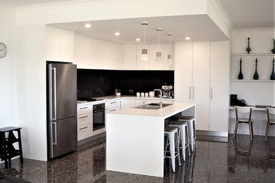 Large modern l-shaped kitchen pantry in Other with a drop-in sink, flat-panel cabinets, white cabinets, laminate benchtops, black splashback, ceramic splashback, stainless steel appliances, concrete floors and with island.