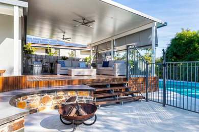 Large backyard deck in Brisbane with a fire feature, a roof extension and mixed railing.