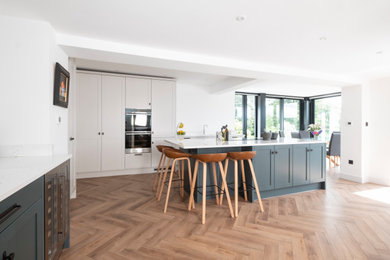 This is an example of a large classic l-shaped kitchen in Cardiff with an integrated sink, shaker cabinets, light wood cabinets, quartz worktops, stainless steel appliances, laminate floors, an island and white worktops.