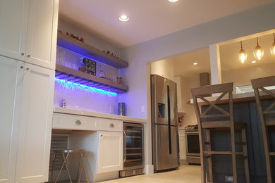 Example of a mid-sized transitional galley travertine floor and beige floor eat-in kitchen design in Miami with shaker cabinets, white cabinets, solid surface countertops, white backsplash, porcelain backsplash, stainless steel appliances, a farmhouse sink and a peninsula