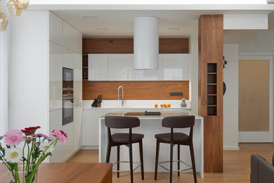 This is an example of a mid-sized contemporary l-shaped open plan kitchen in Other with an integrated sink, flat-panel cabinets, white cabinets, granite benchtops, black appliances, light hardwood floors, with island and white benchtop.