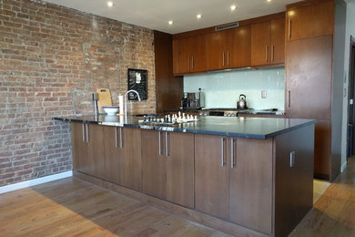 Inspiration for a mid-sized transitional galley medium tone wood floor open concept kitchen remodel in New York with an undermount sink, flat-panel cabinets, white backsplash, glass tile backsplash, stainless steel appliances, a peninsula, dark wood cabinets and soapstone countertops