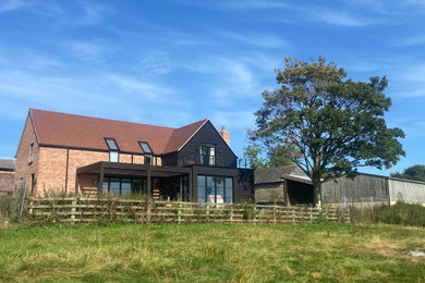 This is an example of a large and black contemporary two floor rear detached house in West Midlands with mixed cladding, a pitched roof, a tiled roof, a red roof and board and batten cladding.