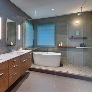 Cette photo montre une salle de bain principale moderne de taille moyenne avec un lavabo encastré, un placard en trompe-l'oeil, des portes de placard en bois brun, un plan de toilette en verre recyclé, une baignoire indépendante, une douche ouverte, un carrelage beige, des carreaux de porcelaine et un sol en carrelage de porcelaine.