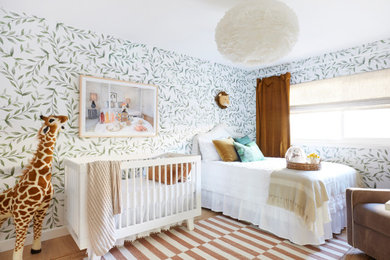 Photo of a transitional gender-neutral nursery in Los Angeles with multi-coloured walls, light hardwood floors, brown floor and wallpaper.