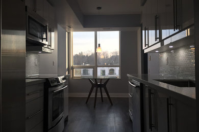 This is an example of a medium sized modern kitchen in Toronto with a submerged sink, flat-panel cabinets, white cabinets, granite worktops, white splashback, glass sheet splashback, stainless steel appliances and vinyl flooring.