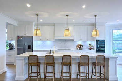 Design ideas for an expansive modern galley eat-in kitchen in Sydney with a farmhouse sink, shaker cabinets, white cabinets, quartz benchtops, white splashback, engineered quartz splashback, black appliances, light hardwood floors, with island, brown floor and white benchtop.