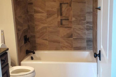 Tub/shower combo - traditional brown tile and porcelain tile porcelain tile tub/shower combo idea in Raleigh with raised-panel cabinets, dark wood cabinets, a two-piece toilet, beige walls, an undermount sink and granite countertops
