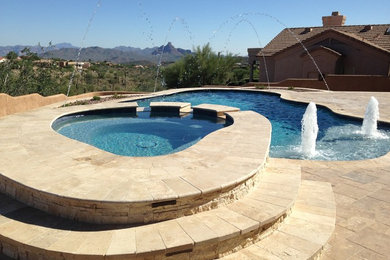 This is an example of a mid-sized contemporary backyard custom-shaped natural pool in Phoenix with a water feature and natural stone pavers.