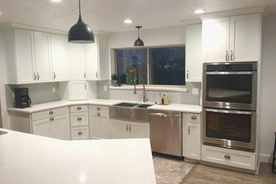 Large traditional u-shaped eat-in kitchen in Orange County with a farmhouse sink, recessed-panel cabinets, white cabinets, quartz benchtops, stainless steel appliances, dark hardwood floors, a peninsula, white splashback, subway tile splashback, brown floor and white benchtop.