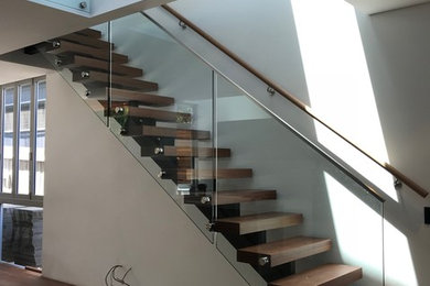 Imagen de escalera recta actual de tamaño medio sin contrahuella con escalones de madera y barandilla de vidrio