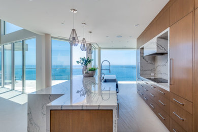 Inspiration for a large contemporary galley limestone floor and beige floor eat-in kitchen remodel in Orange County with a farmhouse sink, flat-panel cabinets, brown cabinets, quartzite countertops, white backsplash, stone slab backsplash, black appliances, an island and white countertops