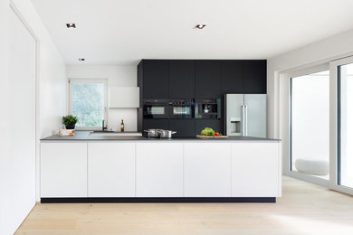 Photo of a large contemporary u-shaped open plan kitchen in Other with flat-panel cabinets, white cabinets, granite benchtops, black appliances, light hardwood floors and a peninsula.