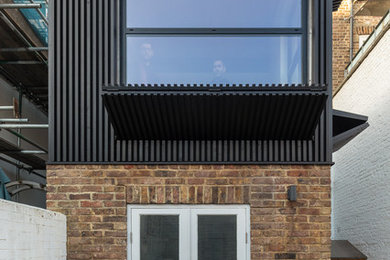 Photo of a small contemporary three-storey black townhouse exterior in London with wood siding, a flat roof and a green roof.