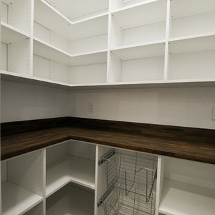 На фото: угловые кухни в стиле кантри с кладовкой, врезной раковиной, фасадами в стиле шейкер, белыми фасадами, столешницей из кварцевого композита, белым фартуком, фартуком из керамической плитки, техникой из нержавеющей стали, полом из ламината, островом и коричневым полом