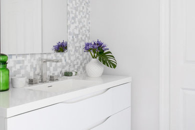 Example of a mid-sized minimalist gray tile and mosaic tile porcelain tile and gray floor bathroom design in New York with flat-panel cabinets, white cabinets, a one-piece toilet, gray walls, an integrated sink, quartz countertops and white countertops