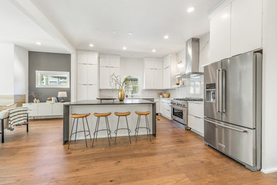 Kitchen - modern brown floor kitchen idea in Charlotte with white cabinets, white backsplash, stainless steel appliances, an island and multicolored countertops