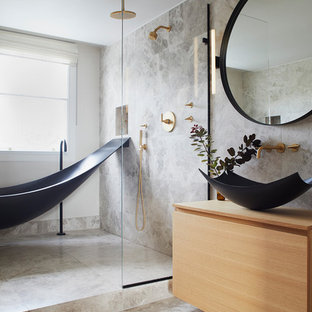 Réalisation d'une salle de bain principale design de taille moyenne avec des portes de placard en bois clair, une baignoire indépendante, un espace douche bain, un WC suspendu, un carrelage gris, du carrelage en pierre calcaire, un mur gris, un sol en calcaire, une vasque, un plan de toilette en bois, un sol gris, aucune cabine, un plan de toilette beige et un placard à porte plane.