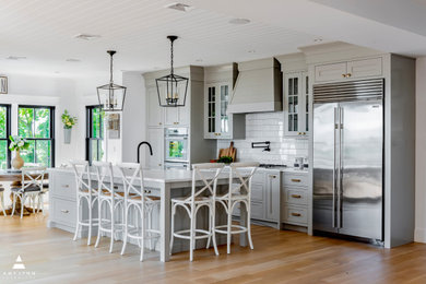 This is an example of a large farmhouse u-shaped kitchen/diner in Boston with a belfast sink, shaker cabinets, grey cabinets, engineered stone countertops, white splashback, ceramic splashback, stainless steel appliances, light hardwood flooring, an island, brown floors, white worktops and a timber clad ceiling.
