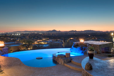 Design ideas for a large contemporary backyard custom-shaped infinity pool in Phoenix with a water feature and decking.