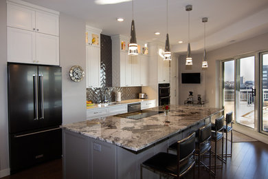 This is an example of a contemporary galley open plan kitchen in Minneapolis with a single-bowl sink, shaker cabinets, white cabinets, granite benchtops, grey splashback, subway tile splashback, stainless steel appliances, medium hardwood floors, with island, brown floor and multi-coloured benchtop.