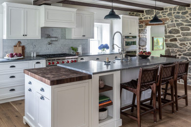 Enclosed kitchen - mid-sized cottage l-shaped light wood floor, brown floor and exposed beam enclosed kitchen idea in Philadelphia with a farmhouse sink, shaker cabinets, white cabinets, quartzite countertops, white backsplash, marble backsplash, stainless steel appliances, an island and gray countertops