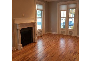 Elegant open concept medium tone wood floor living room photo in Other with gray walls, a standard fireplace and a wood fireplace surround