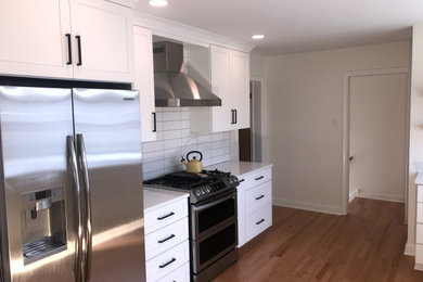Mid-sized transitional u-shaped light wood floor eat-in kitchen photo in Chicago with an undermount sink, flat-panel cabinets, white cabinets, quartz countertops, white backsplash, subway tile backsplash, stainless steel appliances and white countertops