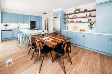 Design ideas for a large transitional eat-in kitchen in Melbourne with a double-bowl sink, shaker cabinets, blue cabinets, quartz benchtops, white splashback, glass sheet splashback, black appliances, medium hardwood floors, with island, brown floor and white benchtop.