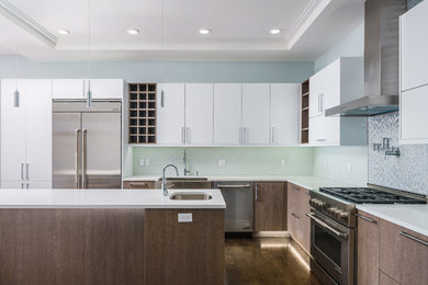 This is an example of a large modern l-shaped eat-in kitchen in New York with a farmhouse sink, flat-panel cabinets, quartz benchtops, white splashback, glass tile splashback, stainless steel appliances, dark hardwood floors, with island, brown floor and white benchtop.
