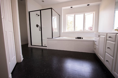 This is an example of a large traditional master bathroom in Orange County with raised-panel cabinets, white cabinets, an alcove tub, an alcove shower, white tile, subway tile, white walls, an undermount sink, black floor and a hinged shower door.