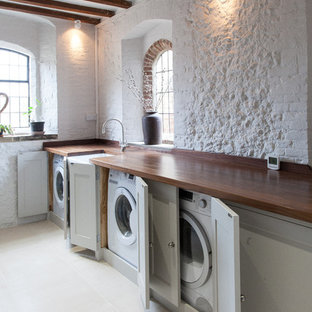 Inspiration for a rural separated utility room in Hampshire with a belfast sink, shaker cabinets, grey cabinets, wood worktops, white walls, a concealed washer and dryer and brown worktops.