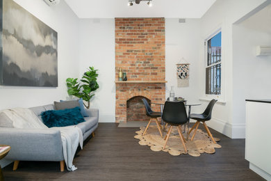 Transitional open concept living room in Melbourne with white walls, dark hardwood floors, a standard fireplace, a brick fireplace surround, no tv and brown floor.