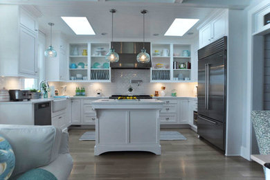 This is an example of a mid-sized beach style u-shaped open plan kitchen in Other with a farmhouse sink, recessed-panel cabinets, white cabinets, quartz benchtops, red splashback, subway tile splashback, stainless steel appliances, light hardwood floors, with island and brown floor.