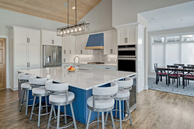 Example of a large transitional l-shaped medium tone wood floor and vaulted ceiling open concept kitchen design in Minneapolis with recessed-panel cabinets, white cabinets, quartz countertops, gray backsplash, glass tile backsplash, stainless steel appliances, an island and white countertops